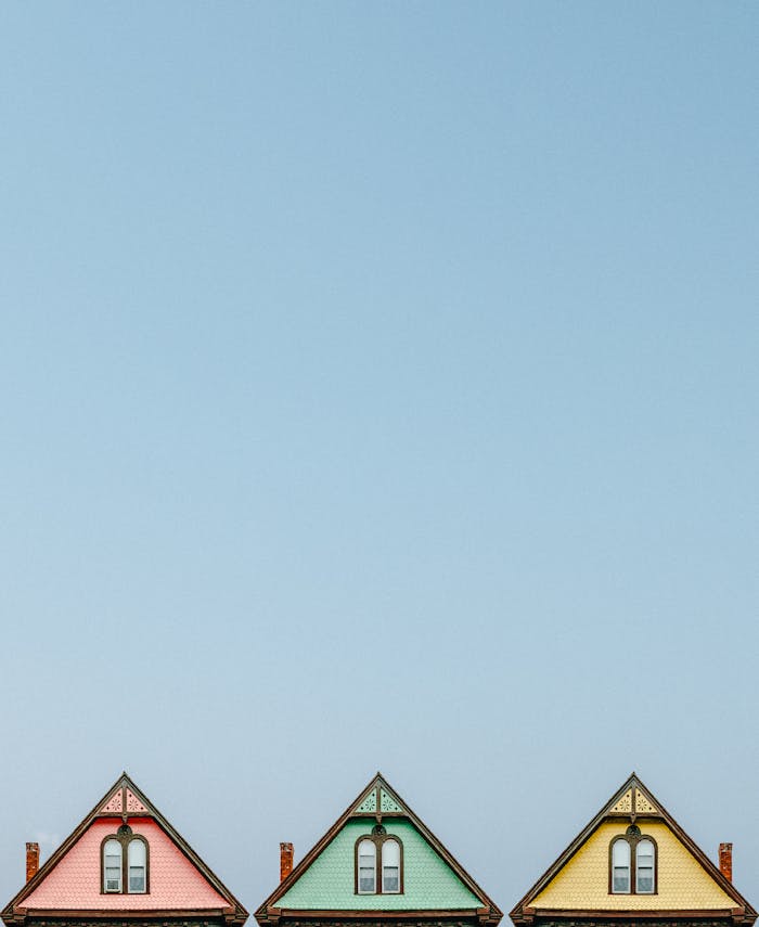 Home Three colorful triangular rooftops against a clear blue sky, showcasing simple architectural design.
